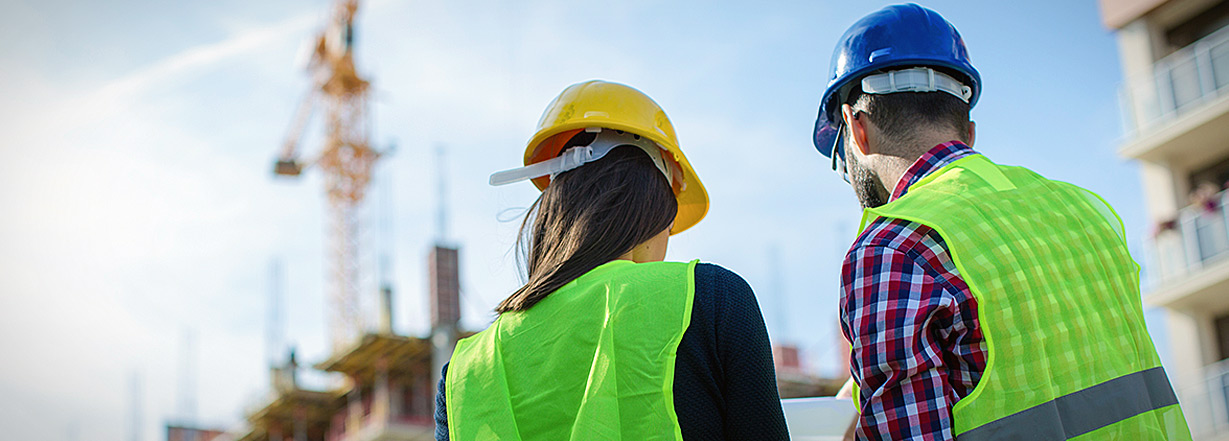 Image of two experts in construction site with safety clothing.